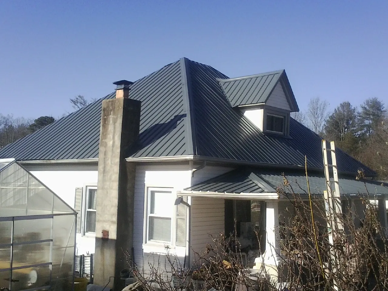 Dark blue standing seam metal roof on a white farmhouse with dormer — Slate & Tile Roof Repair by Roofing Brothers in Maben