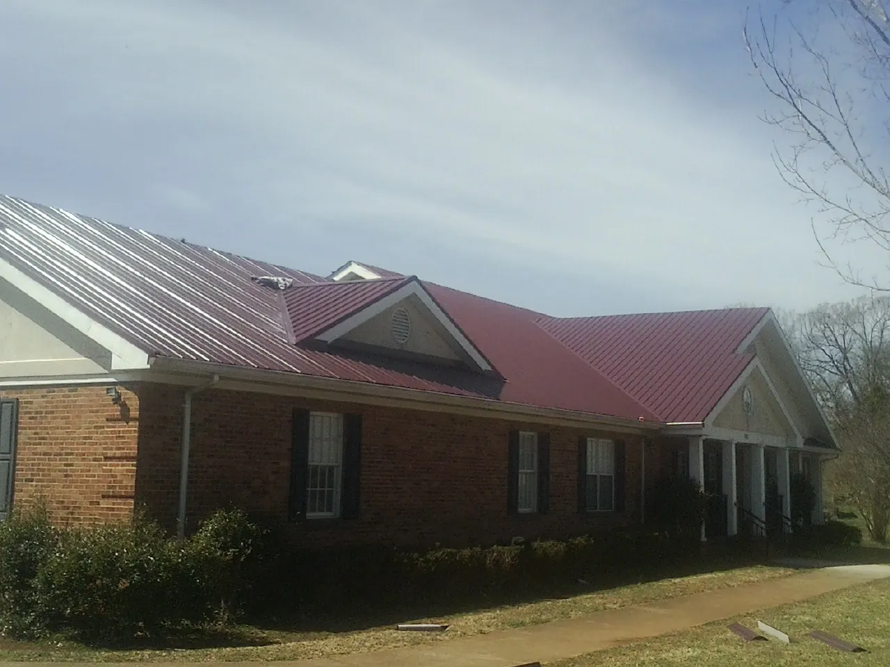 Red metal roof with gabled entries on a long brick building, from a Hail Damage Roof Repair job in Maben