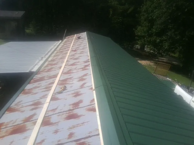 Old rusted panels beside newly installed green metal roofing — Wind Damage Roof Repair by Roofing Brothers in Maben