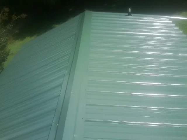 New green metal panels meeting at the ridge of a roof — Flat Roof Repair work by our crew in Maben
