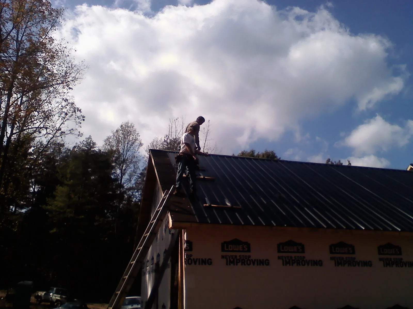 Roofer fastening dark metal panels high against a cloudy sky, from a Roof Inspection job in Maben