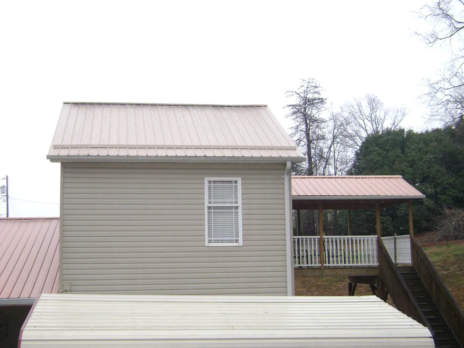 Tan metal roofs on a two story addition and attached porch, from a Roof Replacement job in Maben
